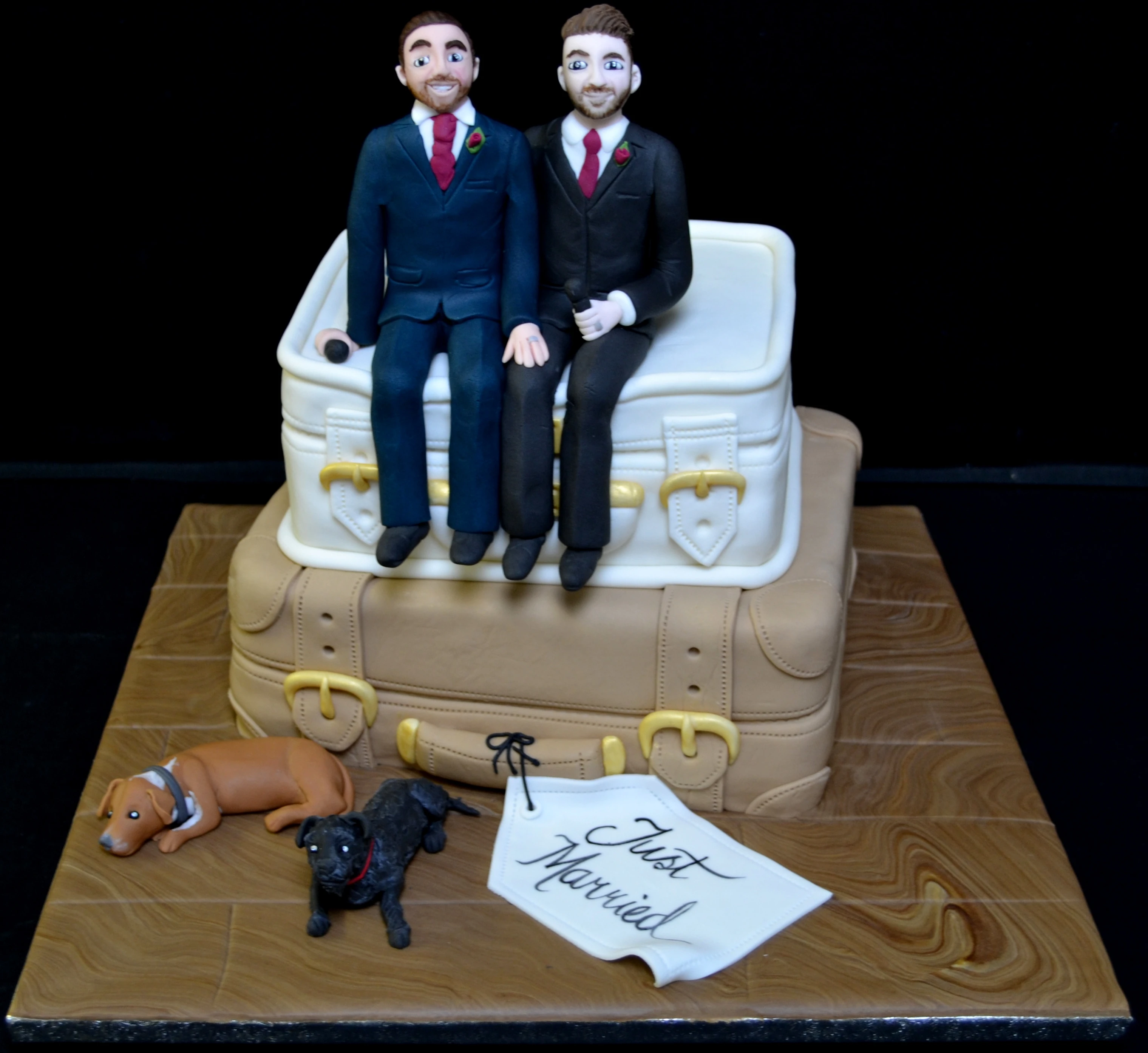 Two-tier wedding cake with sugar paste figures and suitcase design, "Just Married" tag.