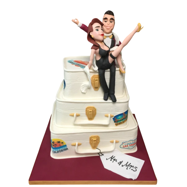 Three-tiered wedding cake with suitcase design and playful sugar paste figures.