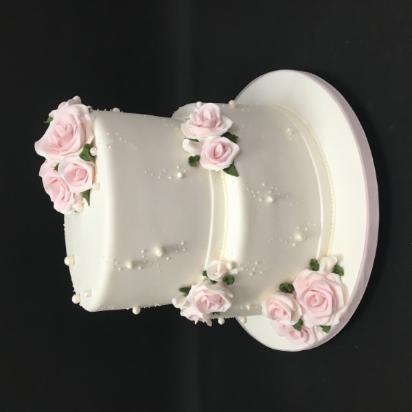 Two-tiered wedding cake with pink sugar roses and pearlescent accents.