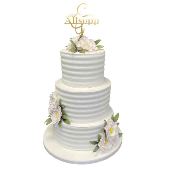 Three-tier white wedding cake with sugar flowers and a golden topper.