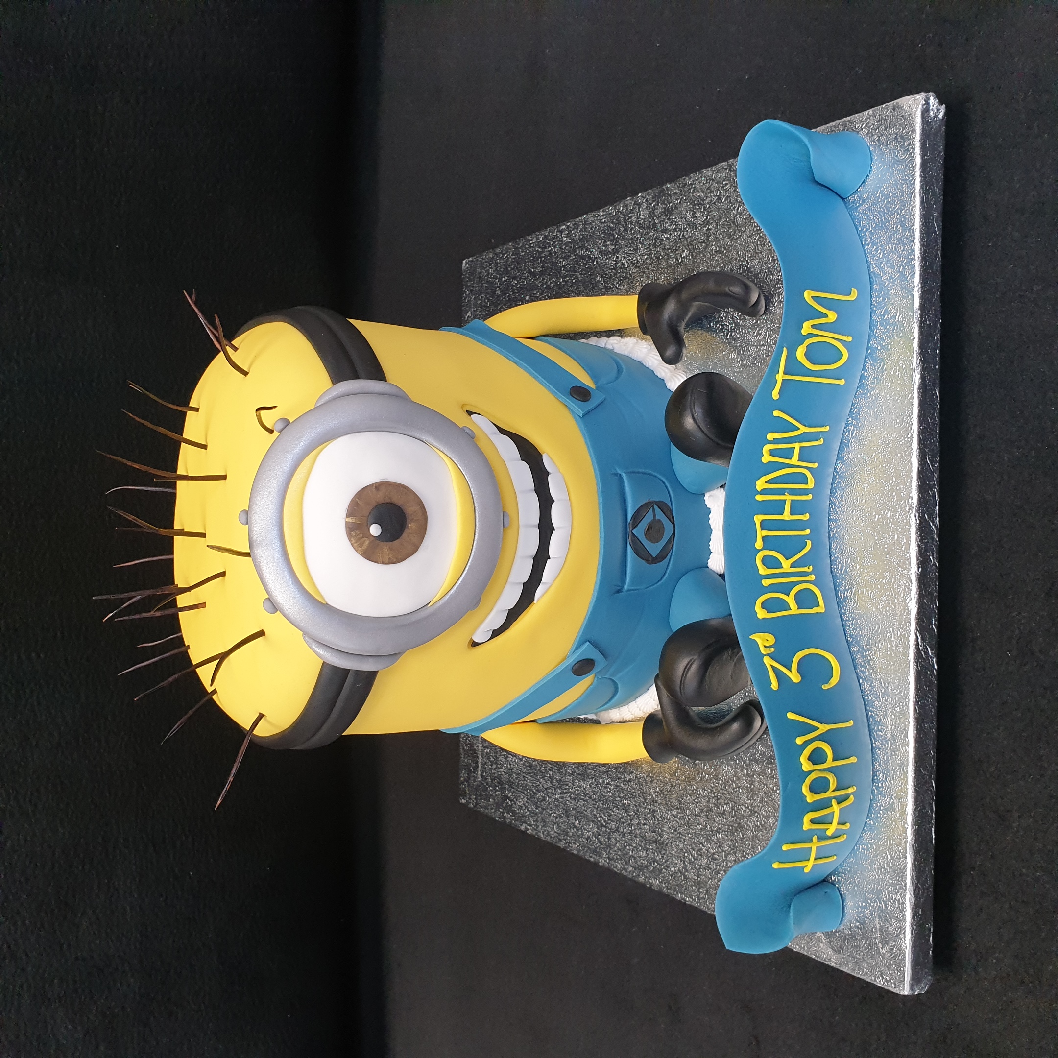 Bespoke Minion-themed celebration cake with yellow fondant and blue overalls, crafted in Solihull, West Midlands.