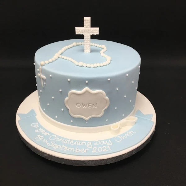 Beautifully decorated Christening cake with white fondant icing, delicate detailing, and a lovely cross on top. Perfect for celebrating a special occasion.
