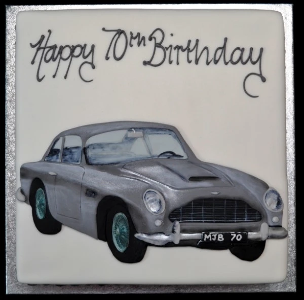 Bespoke cake shaped like a silver Aston Martin DB5 on a square base, crafted in Solihull, West Midlands.