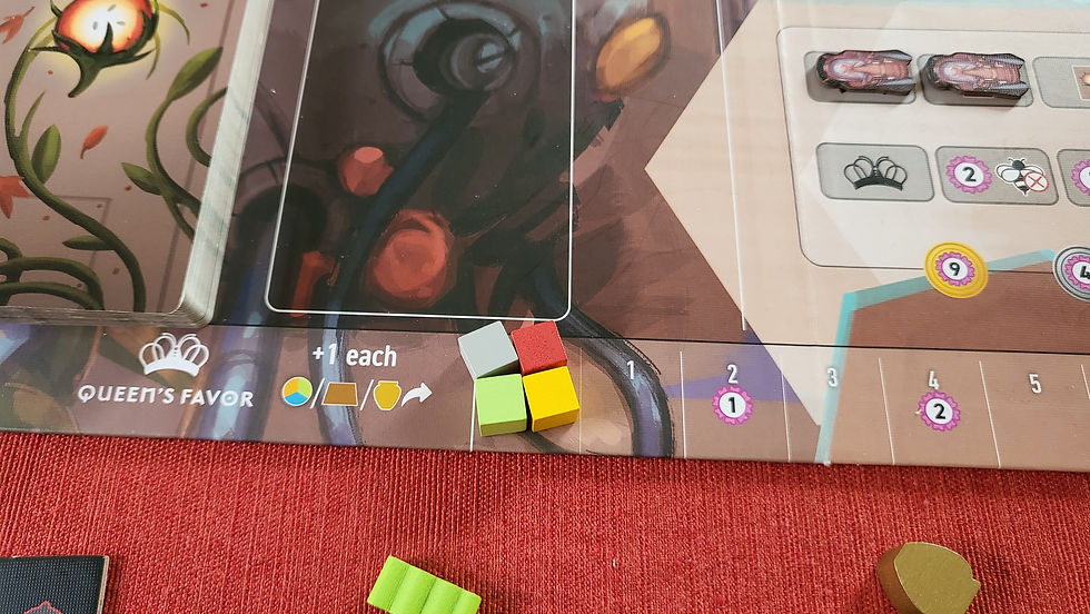 Board game components on a colorful mat; four cubes (gray, red, green, yellow) next to text "Queen's Favor" and icon; floral design.