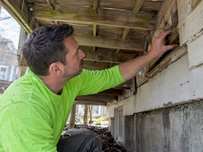 Contractor inspecting a weathered deck ledger