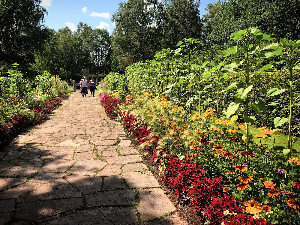 Stenlagd gång i Rottneros Park som ramas in med blommor i rött och orange.