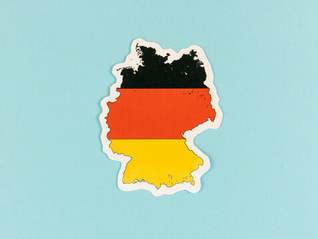 Map-shaped sticker of Germany with the national flag's colors on a light blue background.