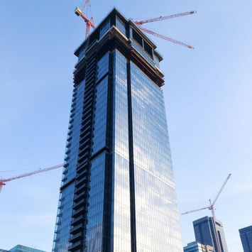 Modern glass skyscraper under construction with cranes.