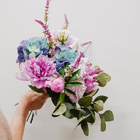 Värikäs silkkikukkakimppu, jossa pioneja, hortensiaa ja vihreitä oksia kädessä 