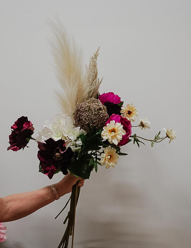 Kädessä pidettävä Burgundy Boho -silkkikukkakimppu vaaleaa taustaa vasten