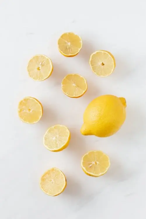 Un citron jaune et des tranches de citrons placés sur une table blanche.