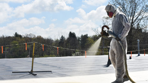Roofing contractor wearing personal protective equipment (PPE) applying spray roof coating to a commercial roof.