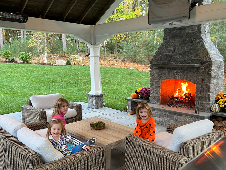 children sitting on wicker furniture in front of an outdoor fireplace.