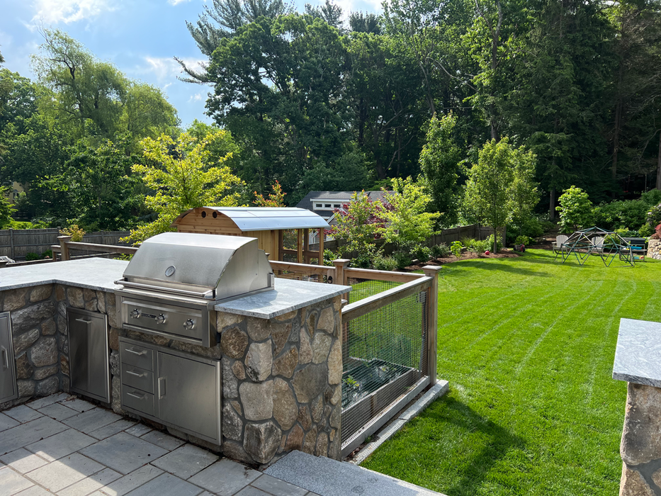 an outdoor kitchen with a grill on top of it with a grassy backyard