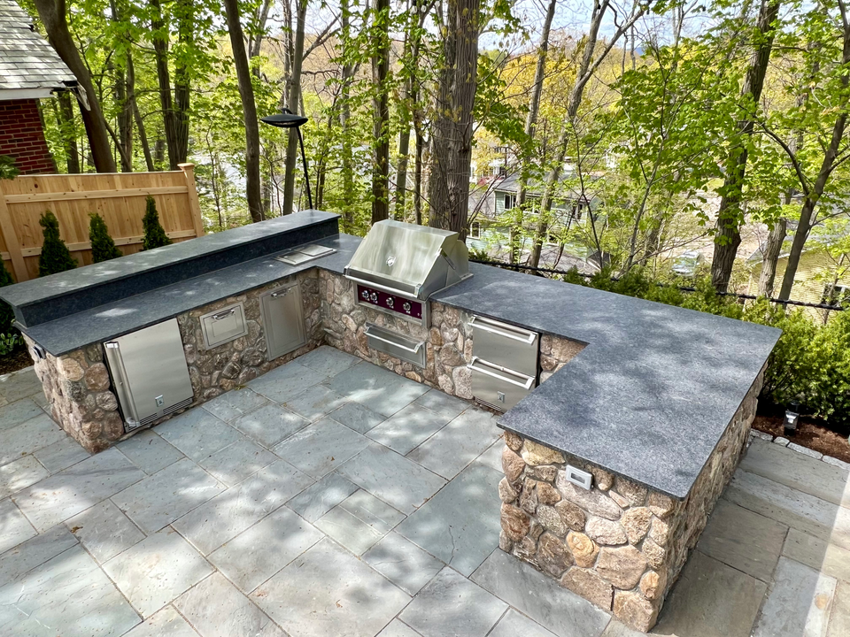 an outdoor kitchen with a grill on top of a stone wall
