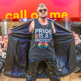 Male performer in dark glasses and  leather trousers opening leather coat and displaying pride is a protest.
