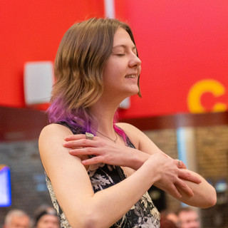 Woman with eyes closed with purple tips to brown hair with arms crossed across chest wearing a black and white sleeveless top.