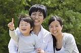 A picture of an Asian American family including a man, a a woman, and a young child, all smiling.