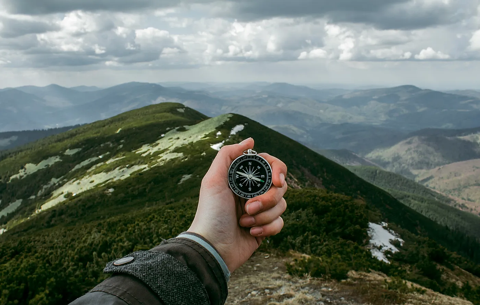 A person holding a compass with a backdrop of an expanse of mountains