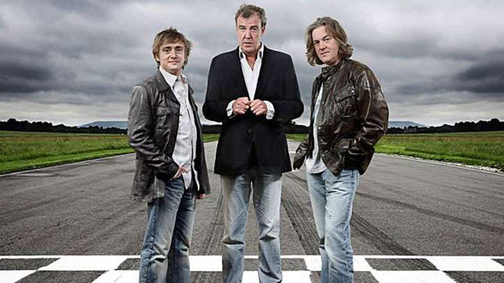 Three former British motoring presenters standing together on a test track, representing the original Grand Tour era