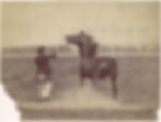 A sepia-toned 1884 photograph by Ottomar Anschütz showing a man in a coat and cap holding a rope attached to a rearing horse in an open field, with a faint grid overlaid on the image.
