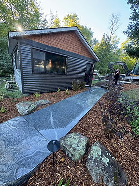 Granite flagstone walkway leading past a lakeside cottage, bordered by natural boulders, mulch, shrubs, and a landscape light