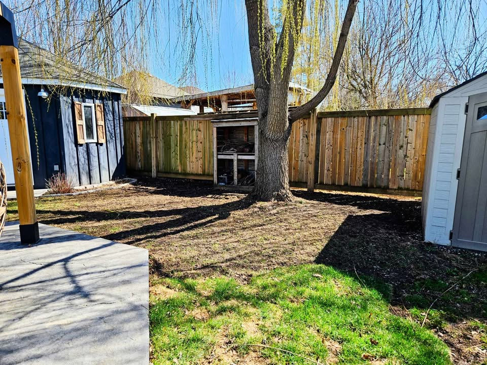 Green grass and dirt clear of debris with a tree, fence and shed in the background.