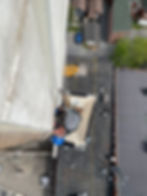 Worker in blue hard hat is suspended on side of building high above ground with ropes doing brick repair.