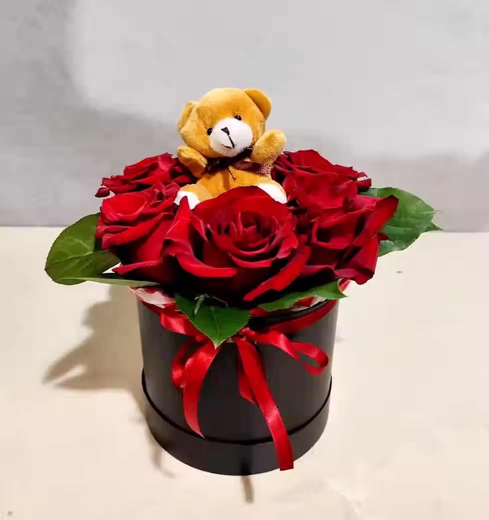 Gift arrangement with vibrant red roses and a cuddly teddy bear in a black luxury box