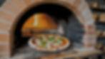 A rustic brick oven with a glowing opening bakes a golden-brown pizza topped with mozzarella and basil.
