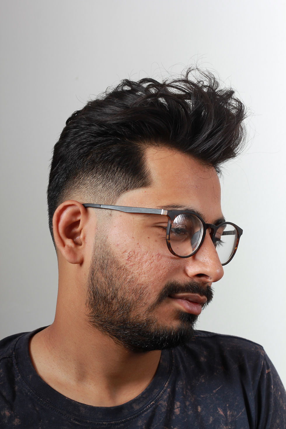 Pánský střih pompadour s medium fade v Barber Street Praha Žižkov. Muž s brýlemi a černými vlasy.