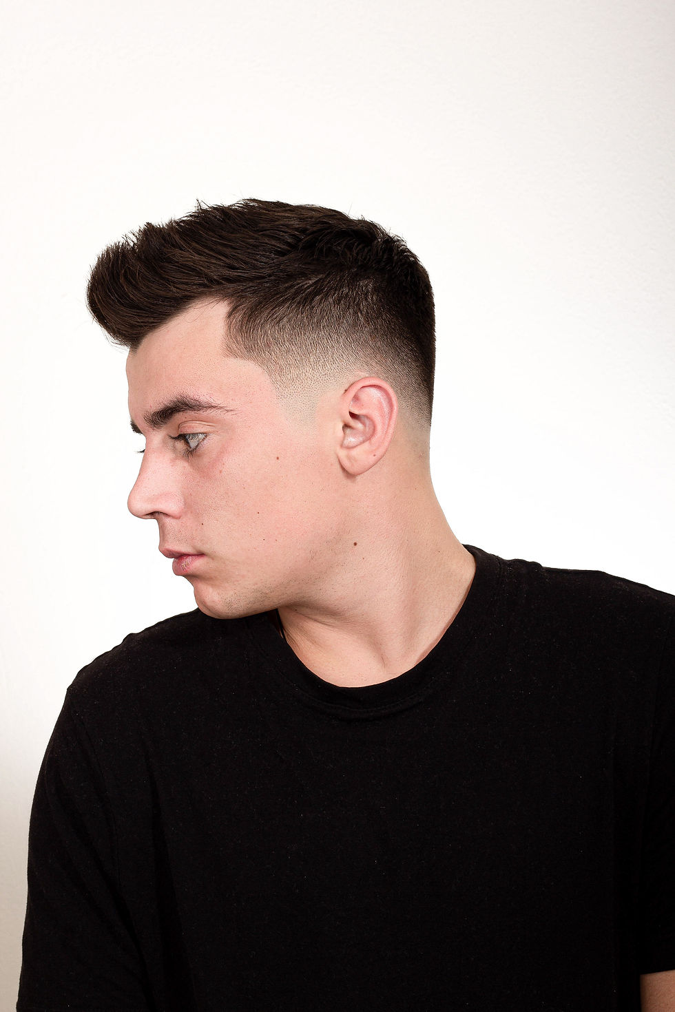 Pánský střih quiff s nízkým přechodem (low fade) v Barber Street Praha Žižkov. Detailní pohled z profilu na muže v černém tričku.