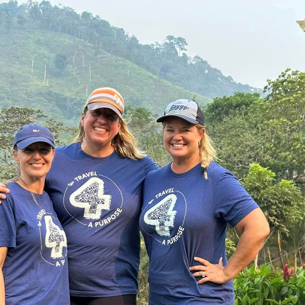 Three women wearing 'Travel 4 a Purpose' shirts stand in front of a lush green hillside on a Honduras mission trip sponsored by Westchase Rotary club.