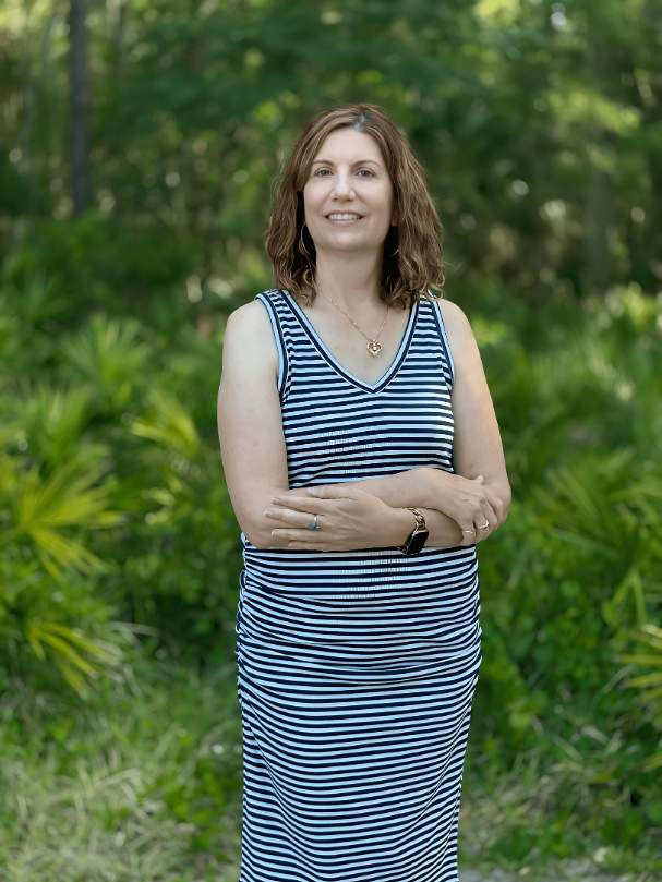 Woman in a striped dress standing outdoors against a background of green foliage