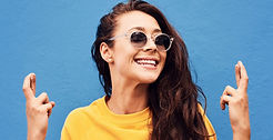 Femme souriante portant un pull jaune et des lunettes de soleil avec les doigts croisés