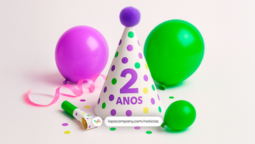 Imagem de festa com fundo branco. No centro, há um chapéu cônico de papel branco com bolinhas coloridas nas cores verde, roxo e amarelo. No chapéu está escrito '2 anos' em roxo. Ao redor, há balões roxos e verdes, um apito de festa com detalhe verde, confetes coloridos e uma fita rosa enrolada. No canto inferior direito, aparece a hashtag '#TheNiver' em roxo.