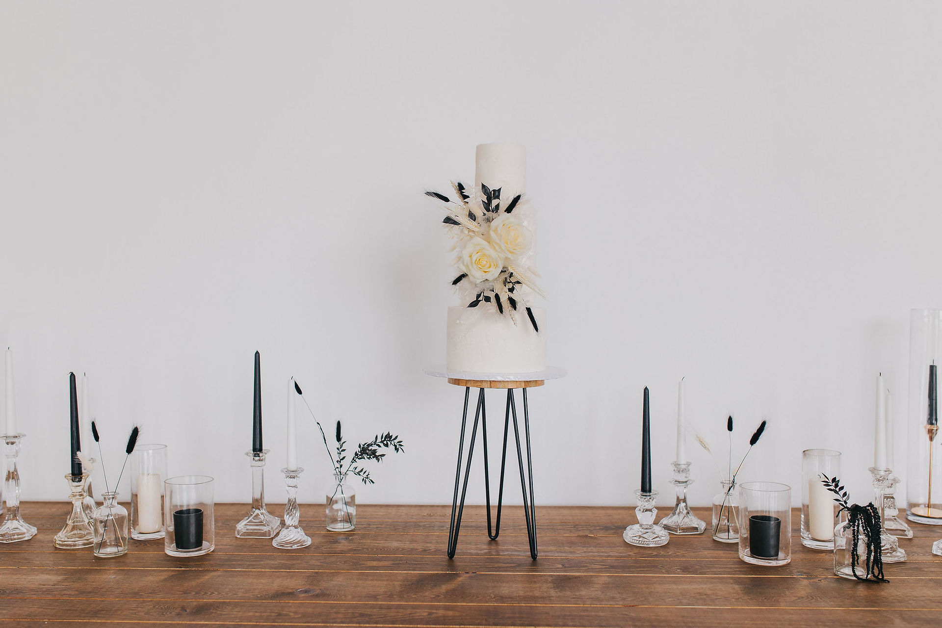 Modern monochrome cake with black and white flowers on a tall black stand. Next to monochrome candles and clear glass vases. weddings cornwall
