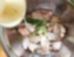 Raw chicken wings with garlic and dill in a metal bowl, being marinated with lemon juice. The scene is bright and fresh.