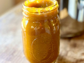 Jar of bright orange pumpkin butter on a wooden surface, next to a shiny metal pot, reflecting a warm and cozy fall kitchen setting.