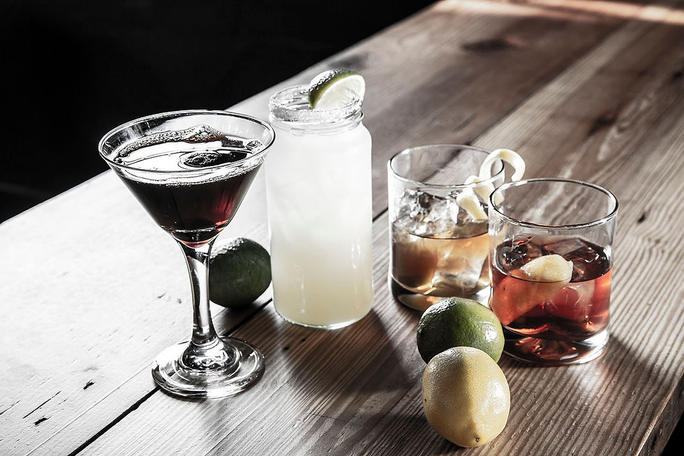 Four beautiful mixed drinks in glasses of varying shapes and sizes garnished with fresh fruit by whole lemons and limes