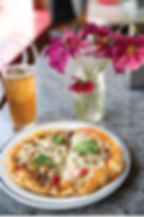 hand tossed personal pizza with basil leaf garnish and herbal bliss tea with mint leaf garnish by bright pink wild flowers