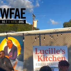 Crowd gathered outside Lucille’s Kitchen during a community event covered by WFAE, featuring mural artwork and local leaders.
