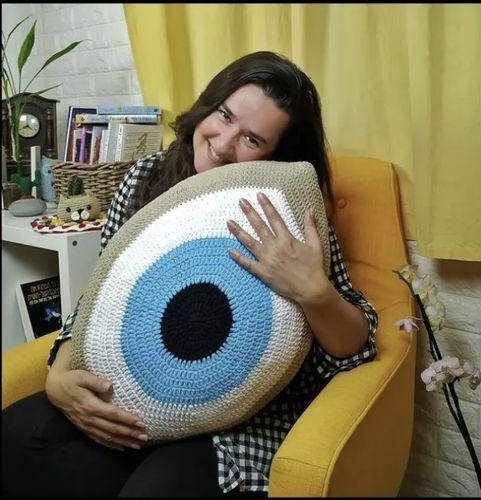 אישה יושבת על כורסה ומחבקת כרית סרוגה בדוגמת עין גדולה