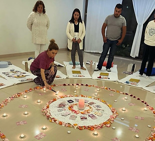 Un grupo de personas al rededor de un circulo de pétalos de rosas, una mujer esta prendiendo una vela. 
