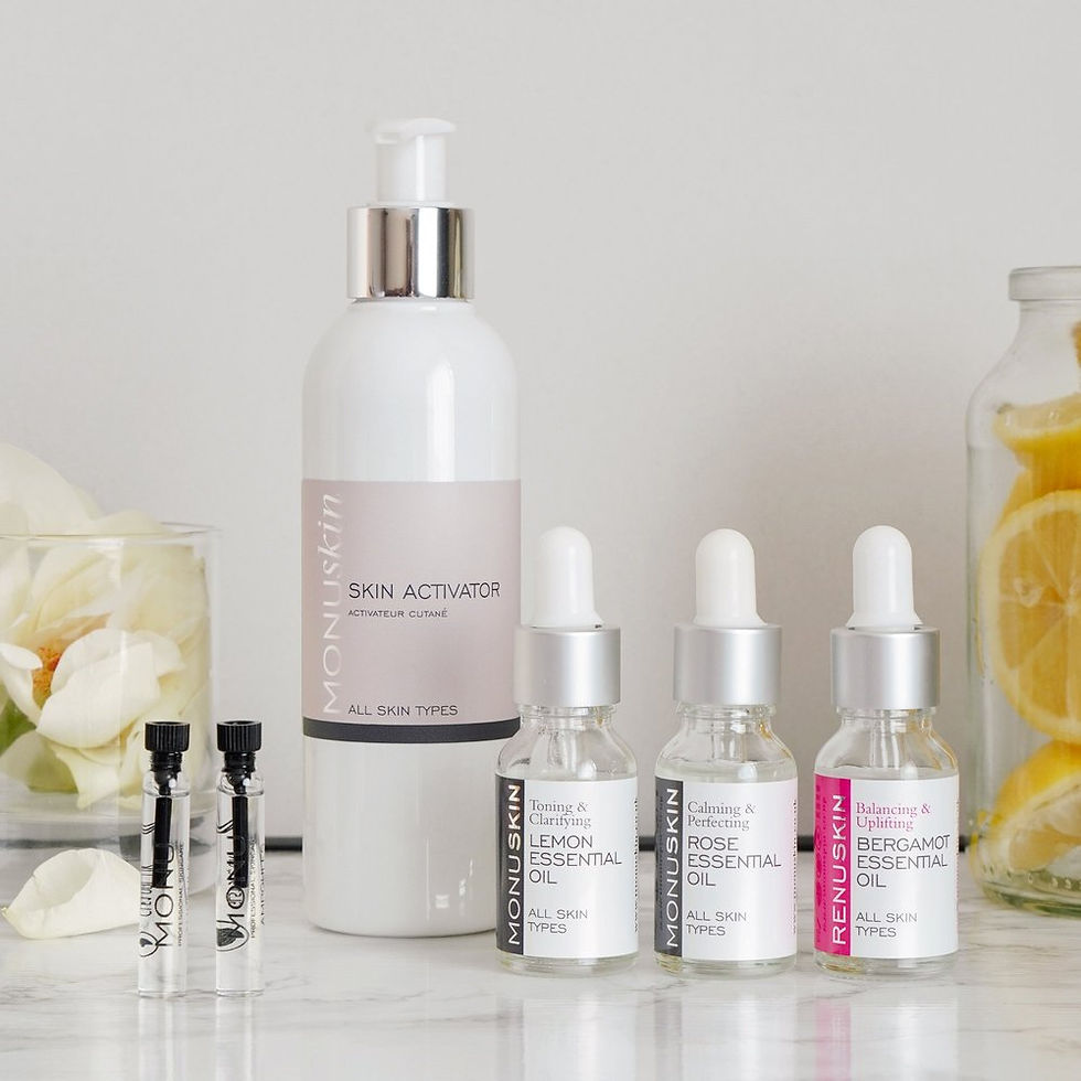Monuskin skincare bottles and droppers on a marble surface, with flower petals and lemon slices in jars in a bright spa setting