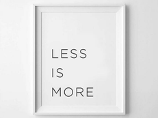 White framed poster on a wall with the text "LESS IS MORE" in simple black font, conveying minimalism and simplicity.