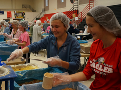 Volunteers wearing hairnets and gloves pack nutritious meal ingredients during a Feed My Starving Children food-packing event hosted by 6:8 Inc.