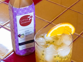 Passionfruit Ginger Ale Fizz in a clear glass cup garnished with an orange slice next to Little Jasmine's Passionfruit Green Tea