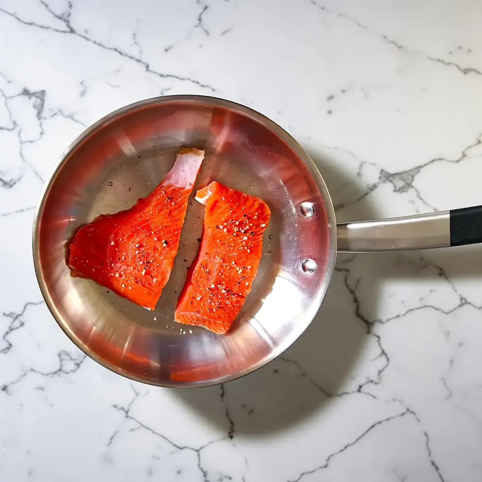 Seasoned raw salmon fillets in a stainless steel pan, prepared for a simple romantic salmon dinner recipe from From Kitchen to Bedroom.