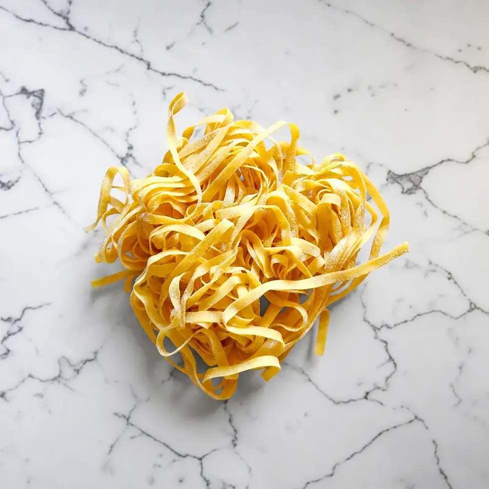 Fresh tagliatelle pasta nest on a white marble counter for From Kitchen to Bedroom cookbook.
